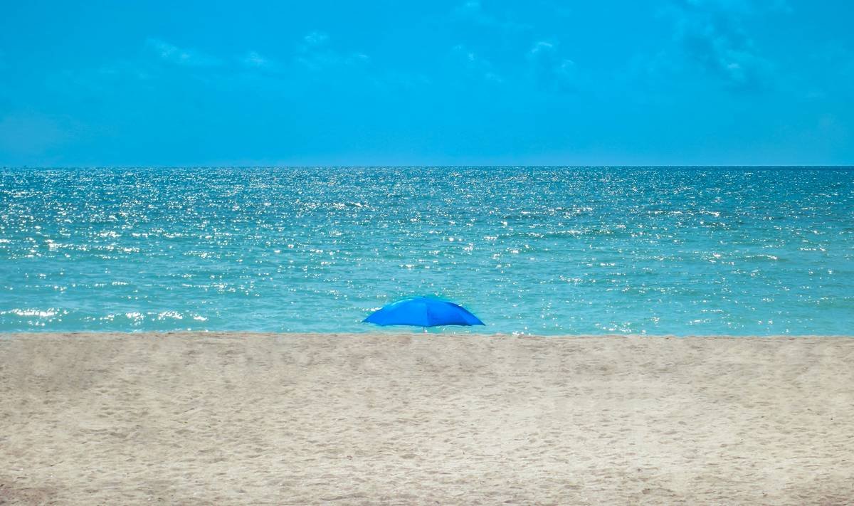 Side-by-side comparison of three Bunnings beach umbrella canopies under simulated rain test showing water beading vs. soaking